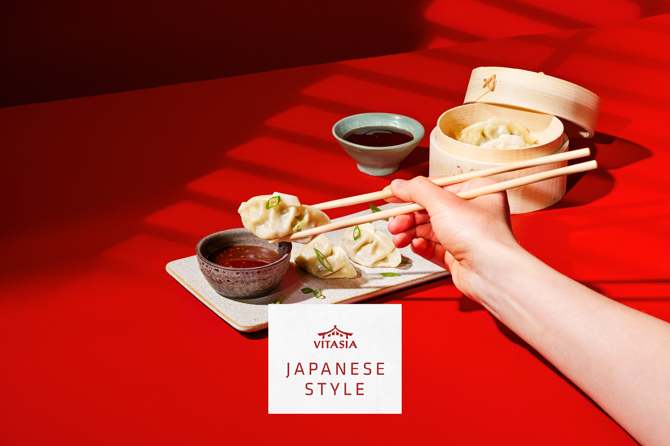 Gyoza giapponesi con salsa, presi con le bacchette, su un tavolo rosso. Stile giapponese.