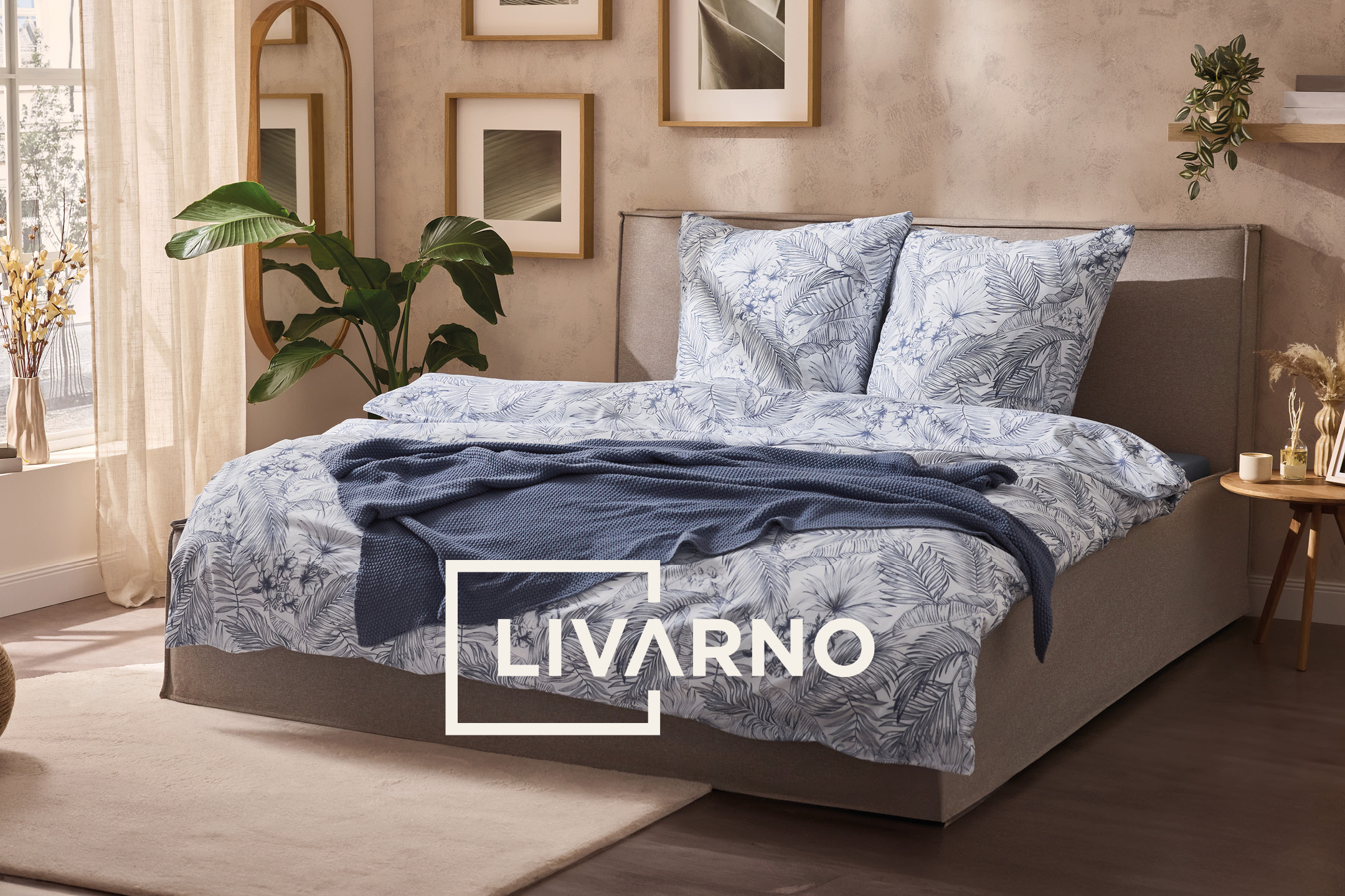 Camera da letto con letto matrimoniale, biancheria da letto a fantasia blu e bianca, e piante.