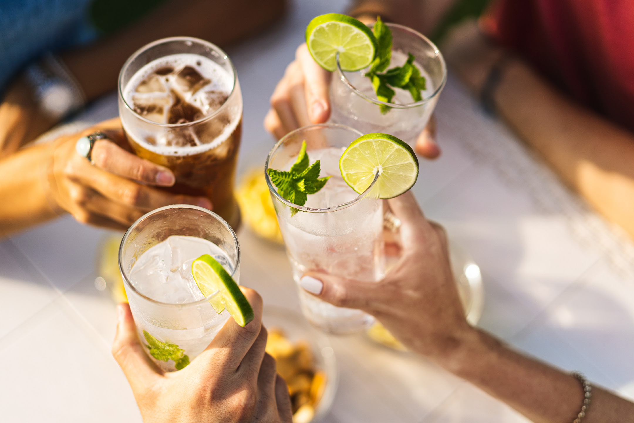Amici brindano con bevande rinfrescanti guarnite con lime e menta, e una birra.