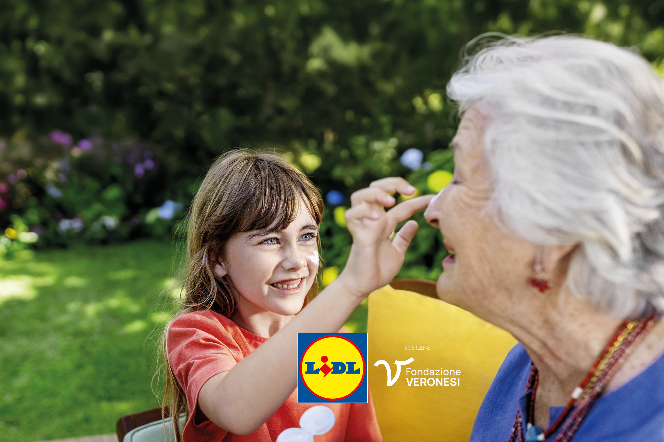 Bambina sorridente applica crema solare sul naso di un'anziana, in un giardino.