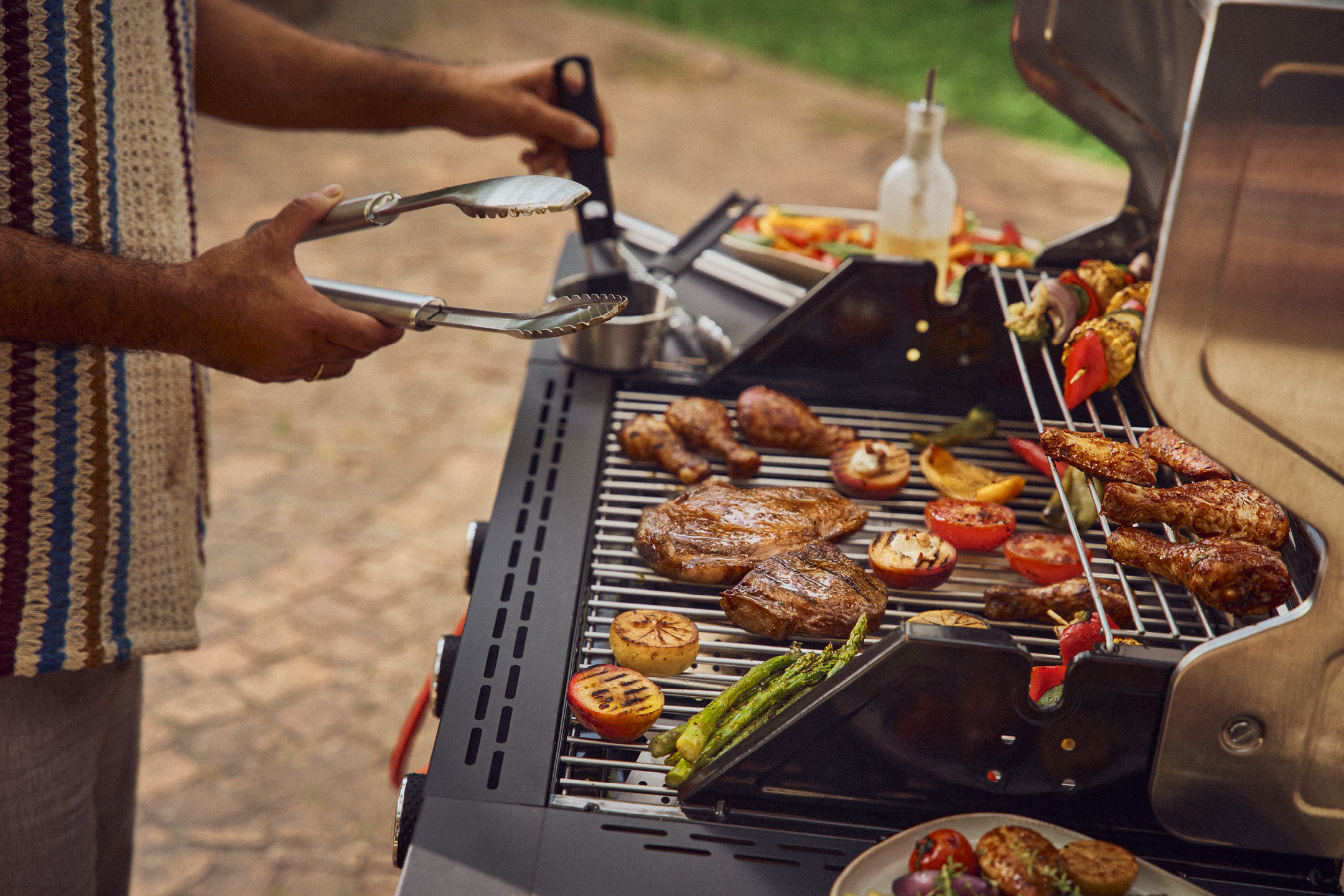 Uomo che griglia carne, verdure e spiedini su un barbecue all'aperto.