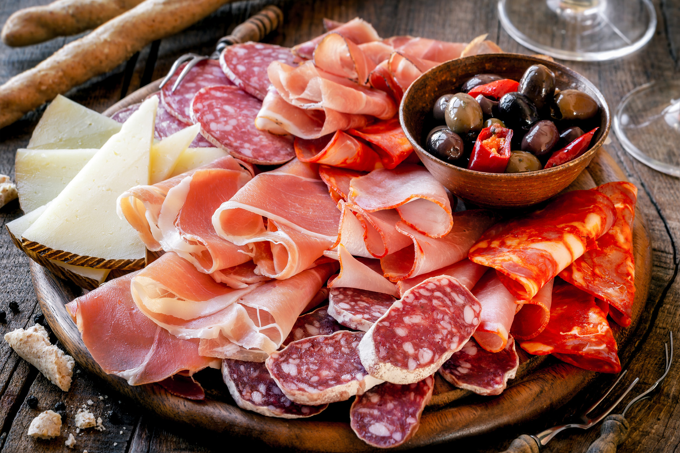 Tagliere di salumi misti, formaggi, olive e peperoncini su tavolo di legno.