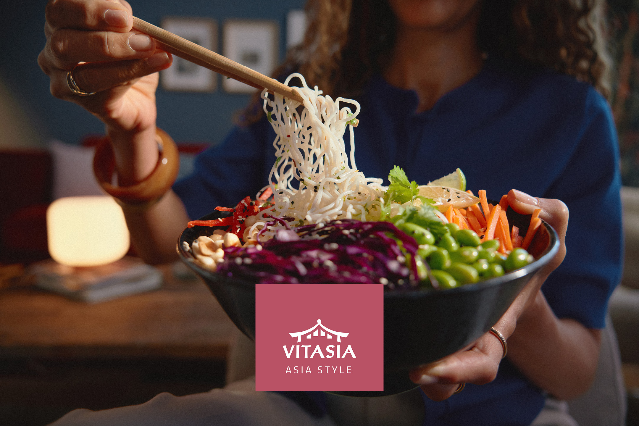 Una persona mangia noodles con verdure fresche da una ciotola, stile asiatico.