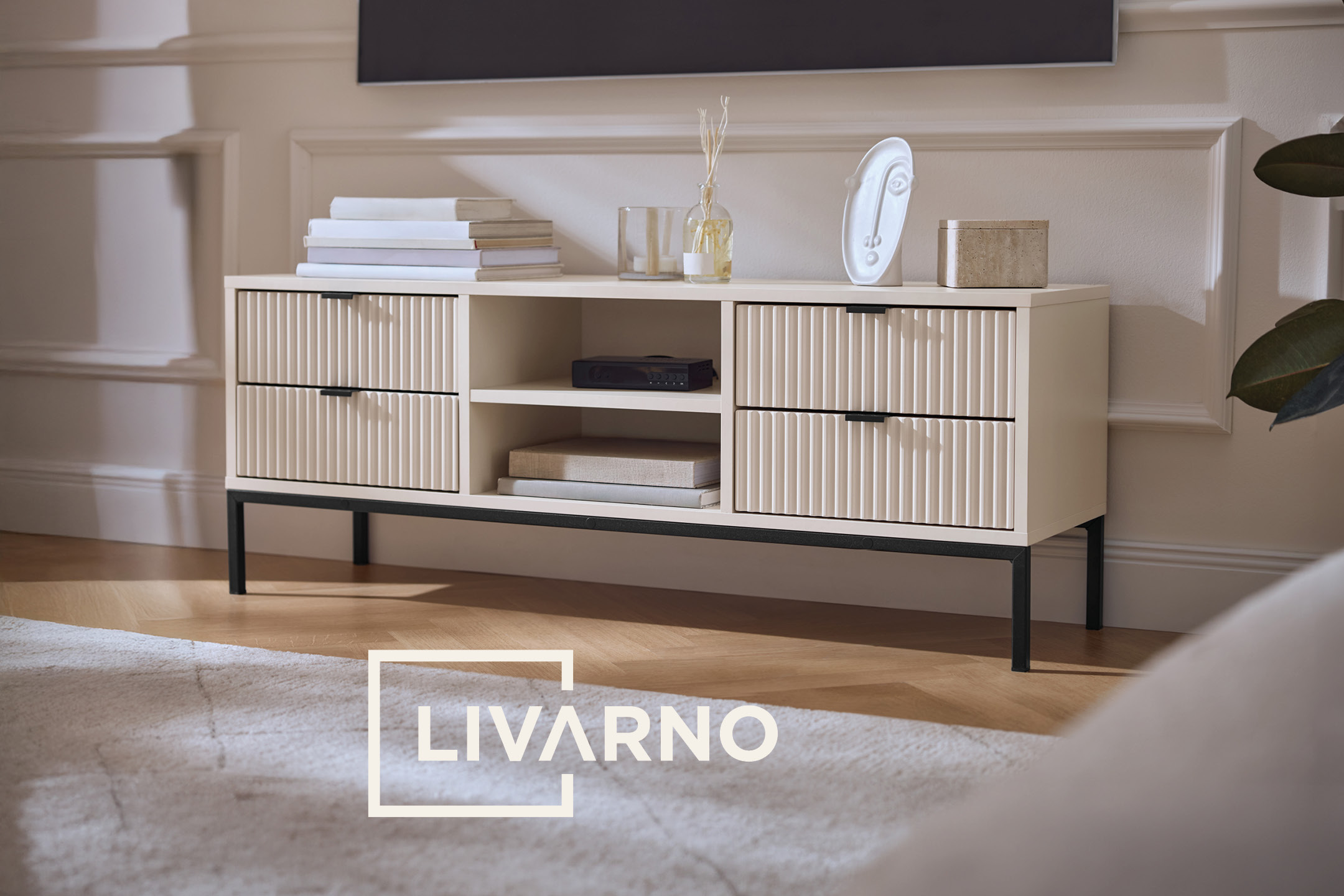 Mobile TV color crema con cassetti a coste, ripiani aperti e decorazioni in un soggiorno moderno.