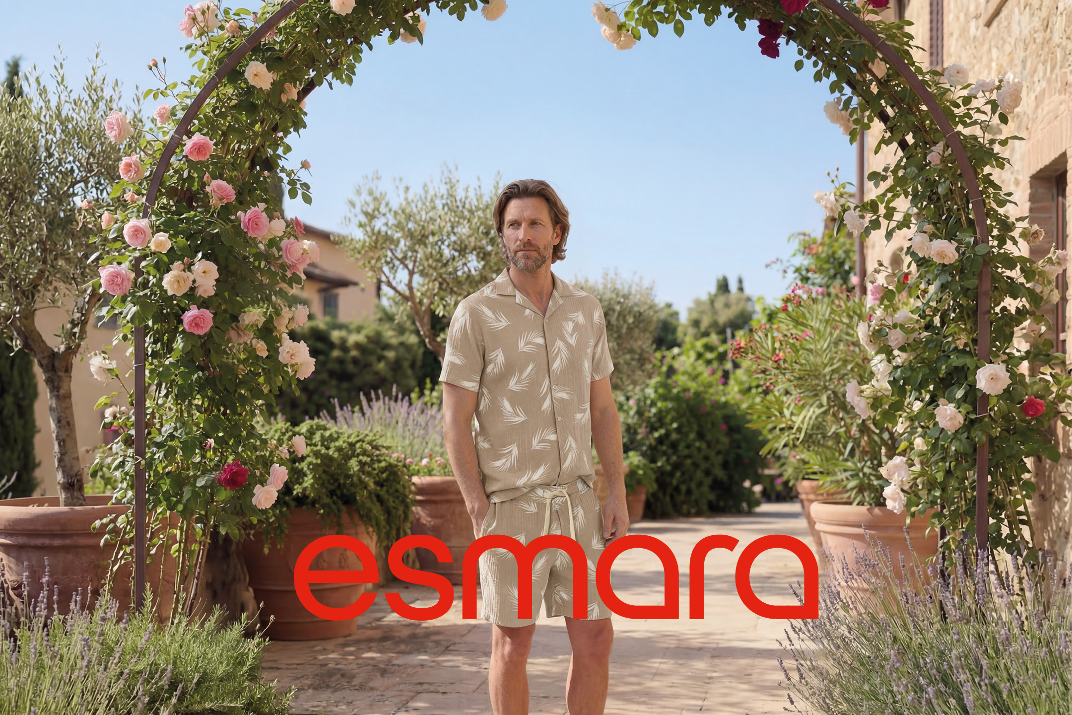 Uomo in completo estivo beige con stampa di foglie, sotto un arco fiorito.