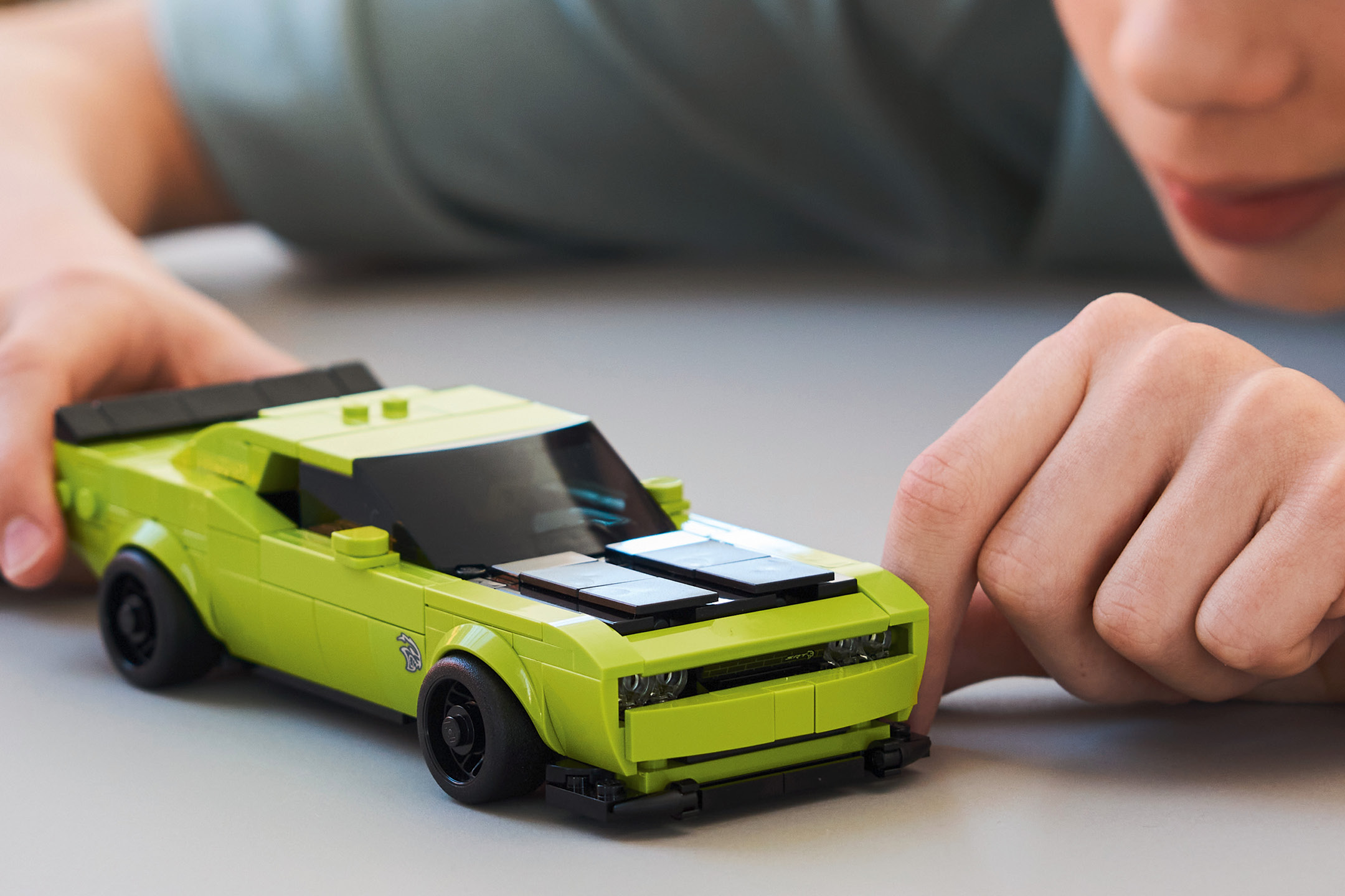 Un bambino gioca con un'auto giocattolo verde brillante su una superficie grigia.