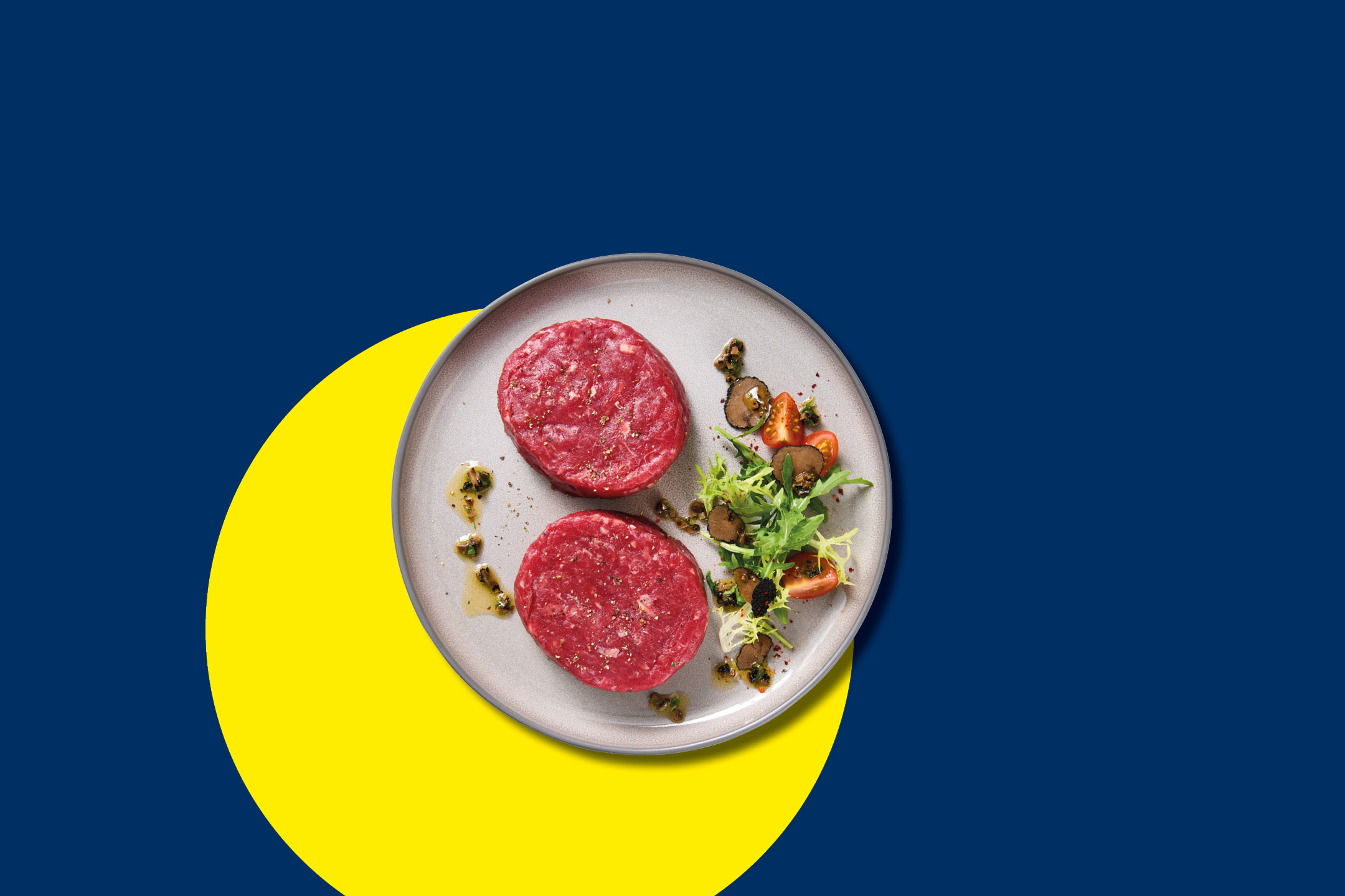 Due hamburger di carne cruda con insalata e pomodorini su un piatto, sfondo blu e giallo.