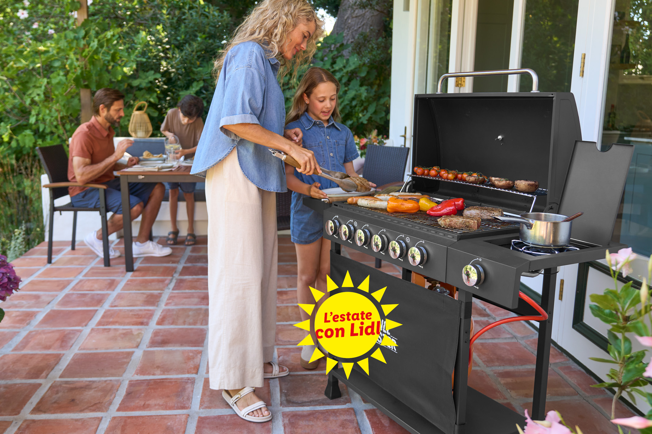 Famiglia che fa un barbecue all'aperto con carne, verdure e salsicce. Testo: 'L'estate con Lidl'.