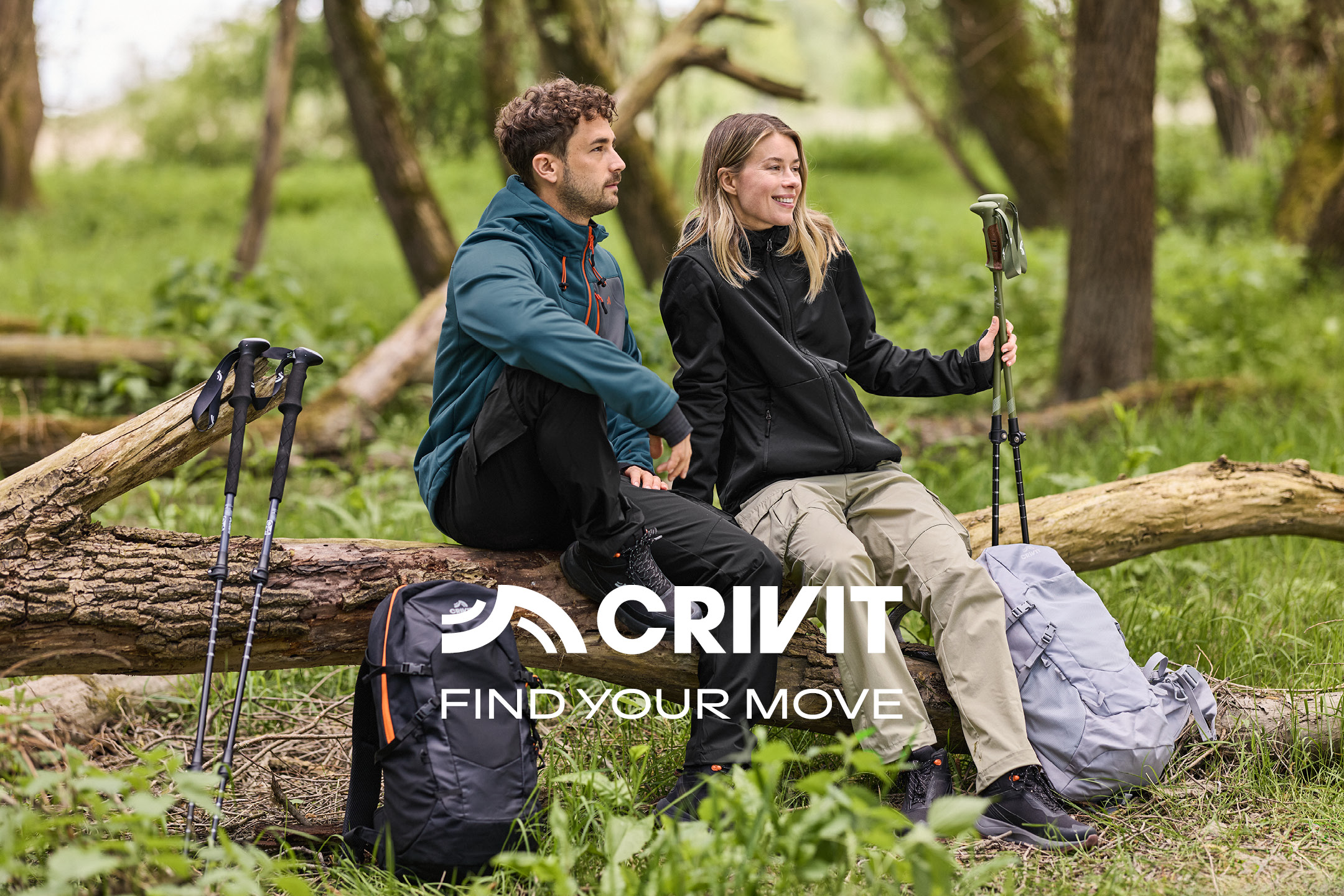 Due escursionisti con bastoncini da trekking, giacche sportive, seduti su un tronco d'albero. Testo: FIND YOUR MOVE.
