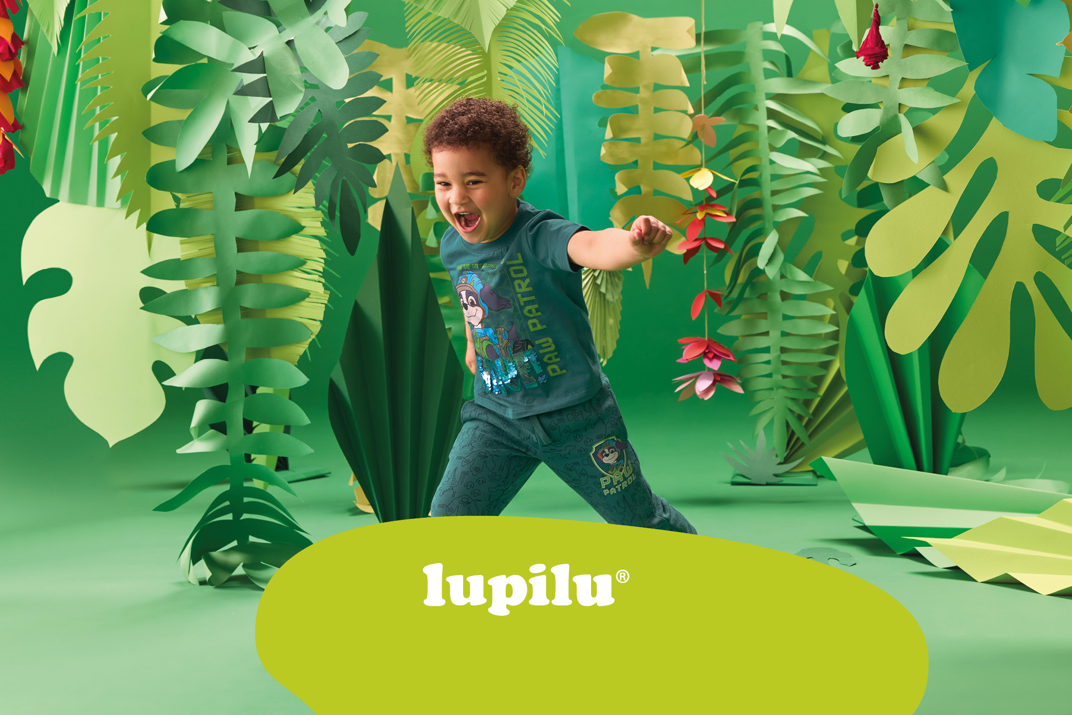 Un bambino sorridente con una maglietta Paw Patrol in un ambiente giungla di carta.