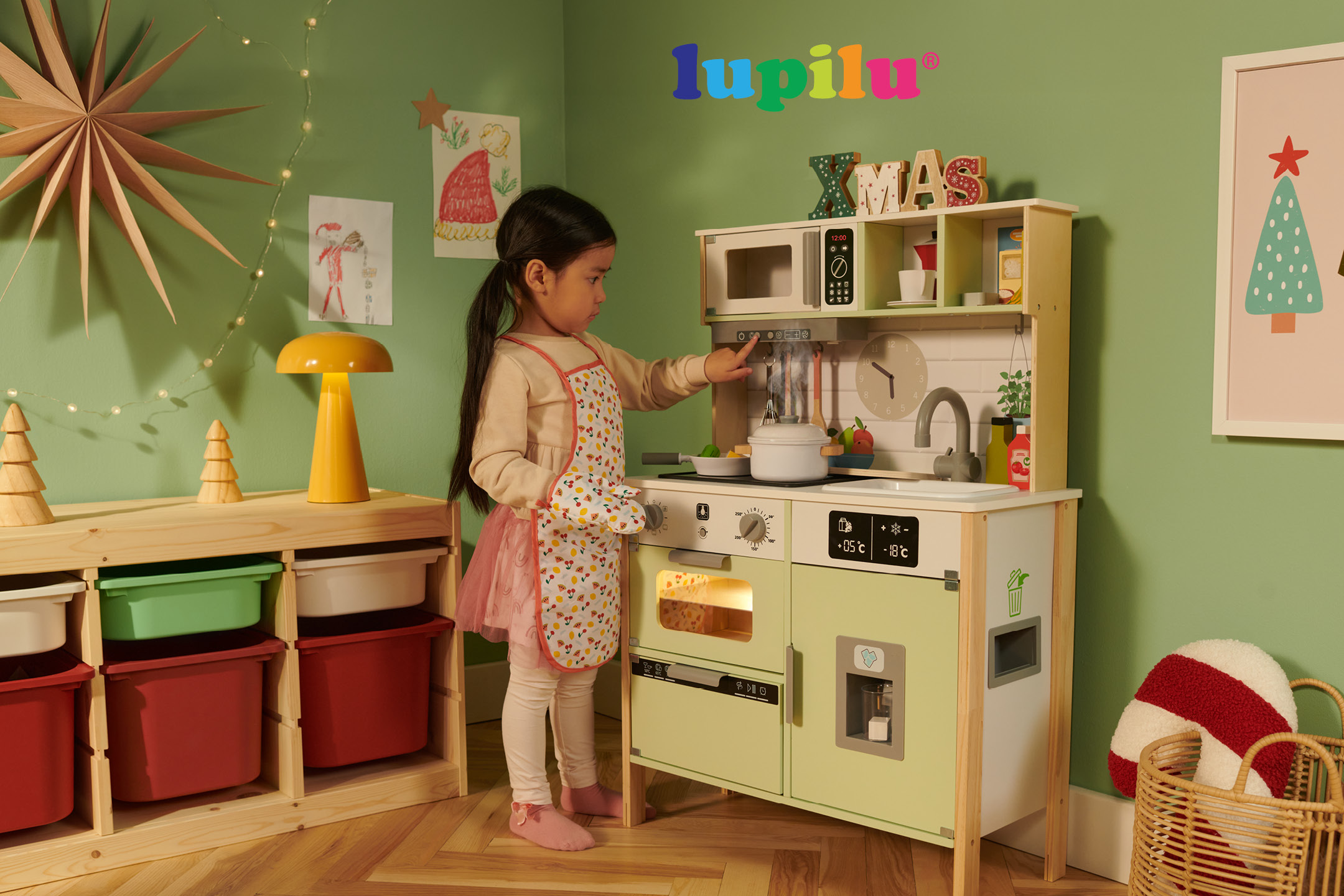 Bambina gioca con una cucina giocattolo in legno attrezzata con accessori.