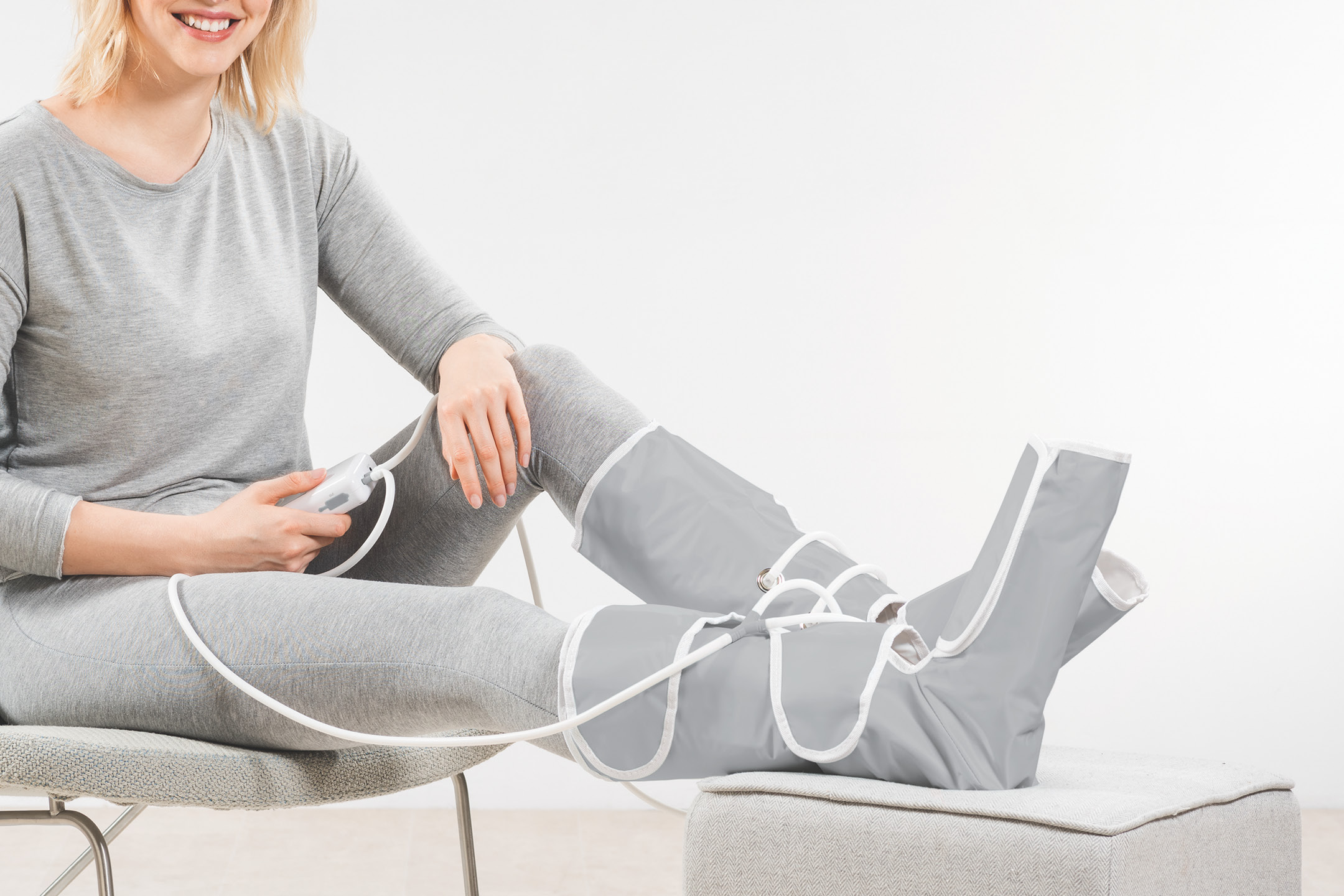 Donna seduta che utilizza un massaggiatore pressoterapico per gambe e piedi con telecomando.