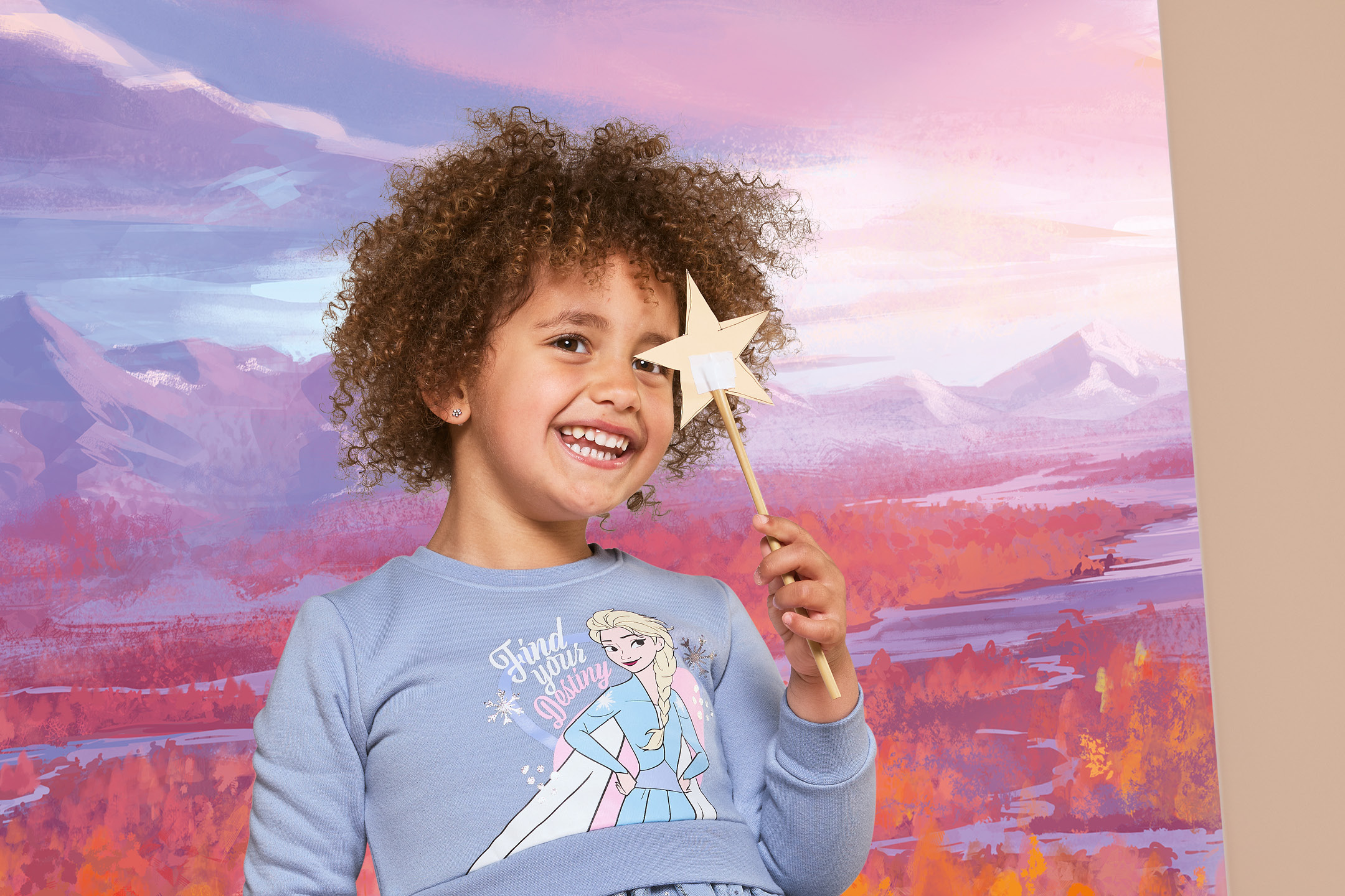 Bambina sorridente con capelli ricci che tiene in mano una bacchetta a forma di stella.
