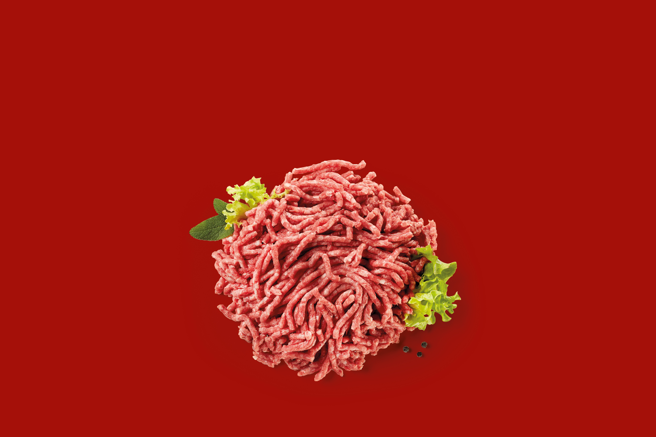 Carne macinata fresca con foglie di lattuga e grani di pepe su sfondo rosso.