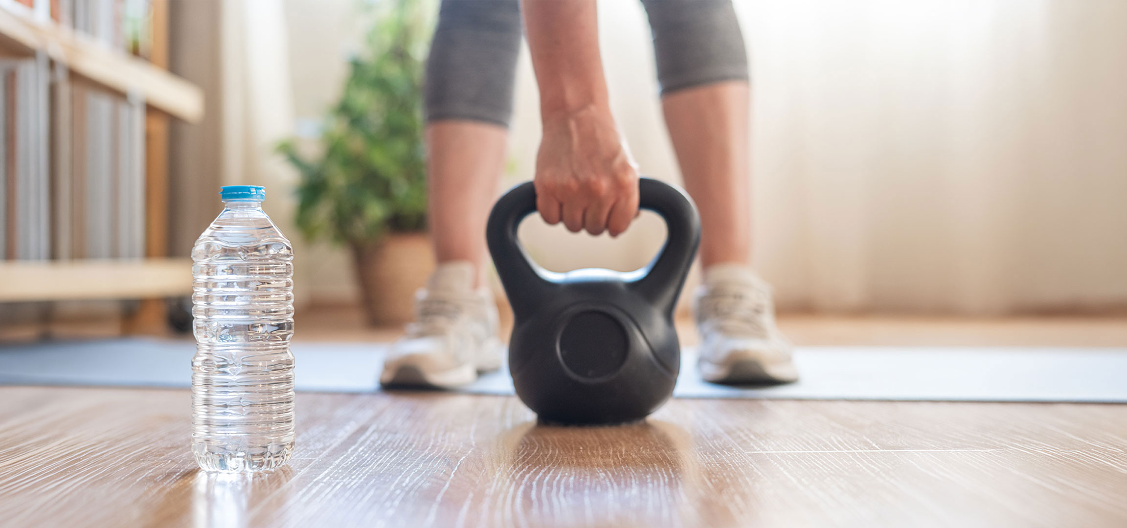 aiLabeling.aiLabelForImageAltText: Donna si prepara ad allenarsi con un kettlebell e una bottiglia d'acqua su un tappetino da yoga.