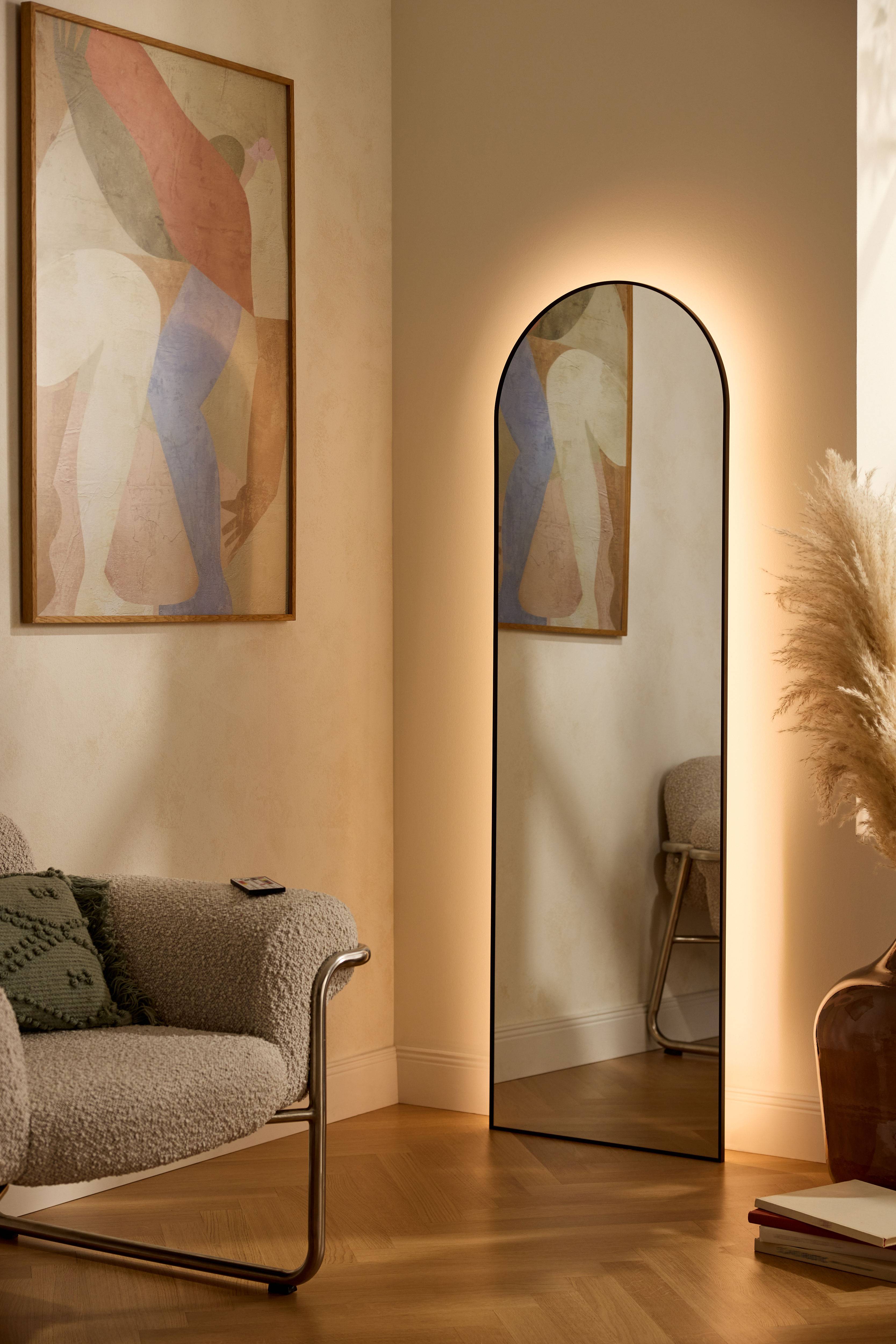 Specchio illuminato e quadro astratto in un soggiorno moderno con poltrona e erba della pampa.