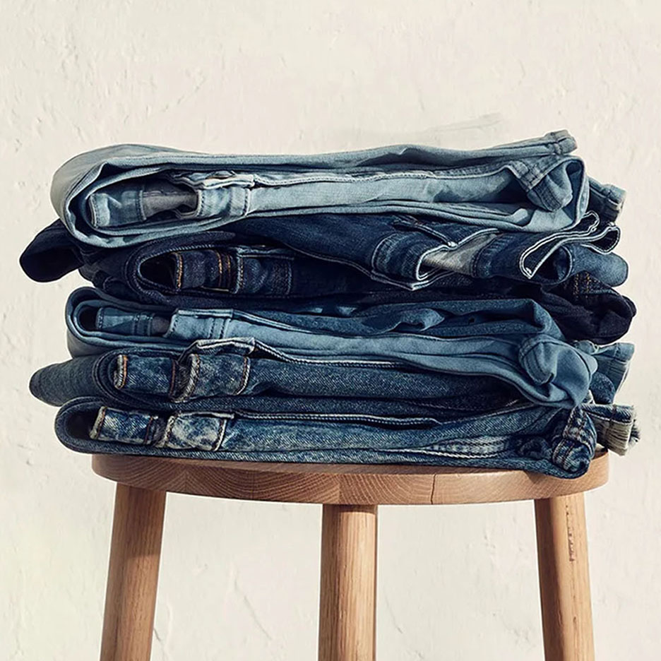 Una pila di jeans di diverse sfumature di blu su uno sgabello di legno.