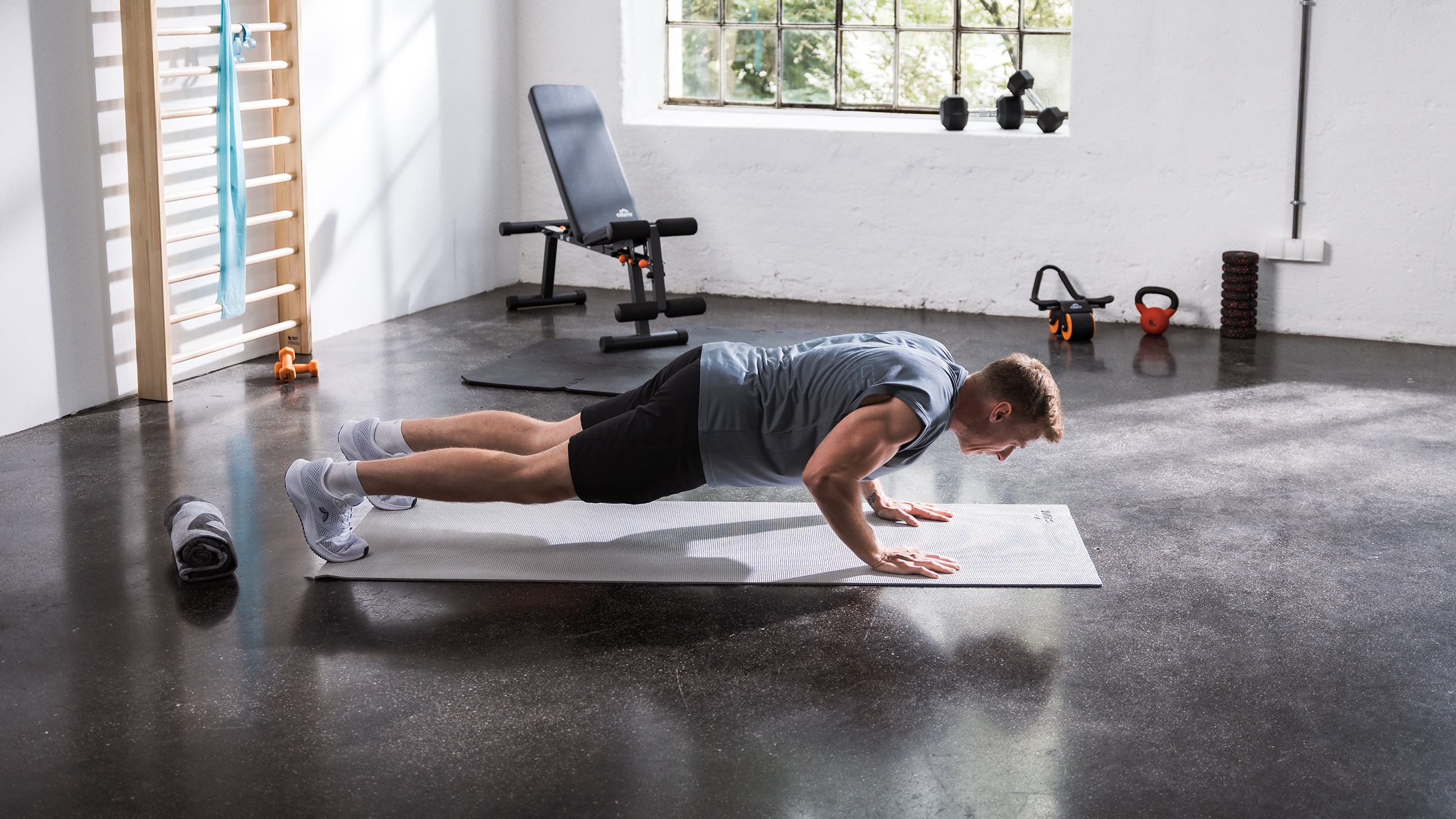 Uomo che fa flessioni su un tappetino in una palestra domestica con varie attrezzature fitness.