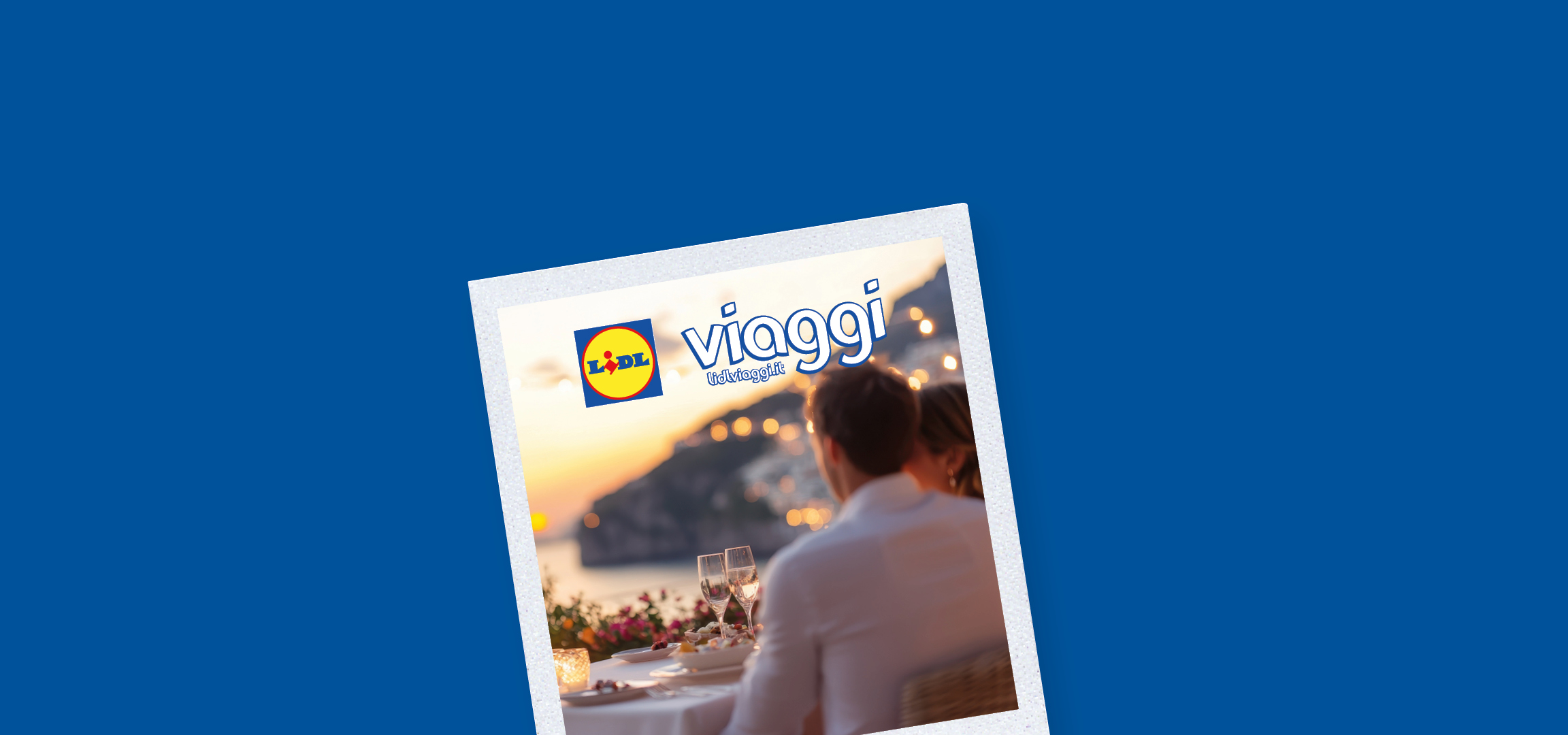 Coppia che brinda con calici di spumante al tramonto, con vista mare e luci sfocate.