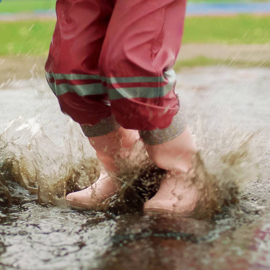 Bambino con pantaloni impermeabili rossi e stivali che salta in una pozzanghera.