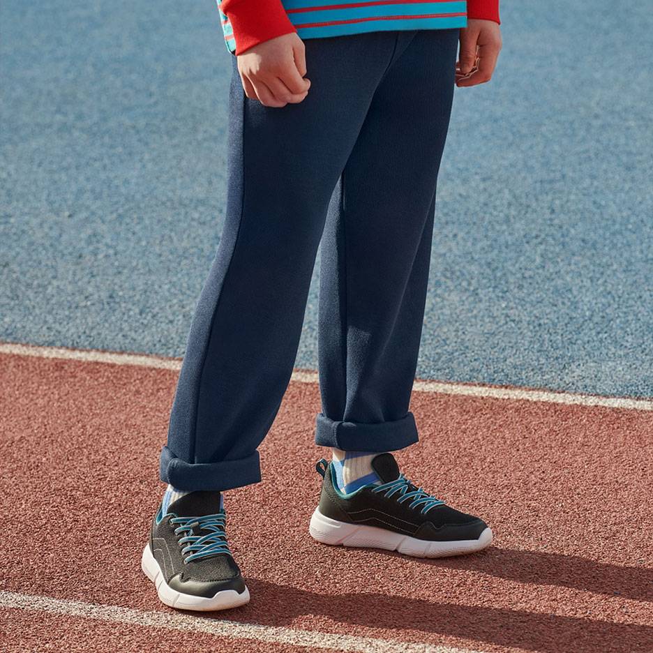 Pantaloni della tuta blu navy e sneakers nere con lacci blu su una pista da corsa.