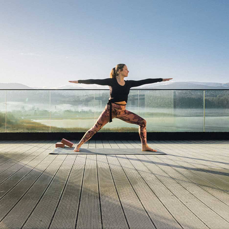 Donna in leggings e top sportivi che fa yoga su una terrazza con vista.
