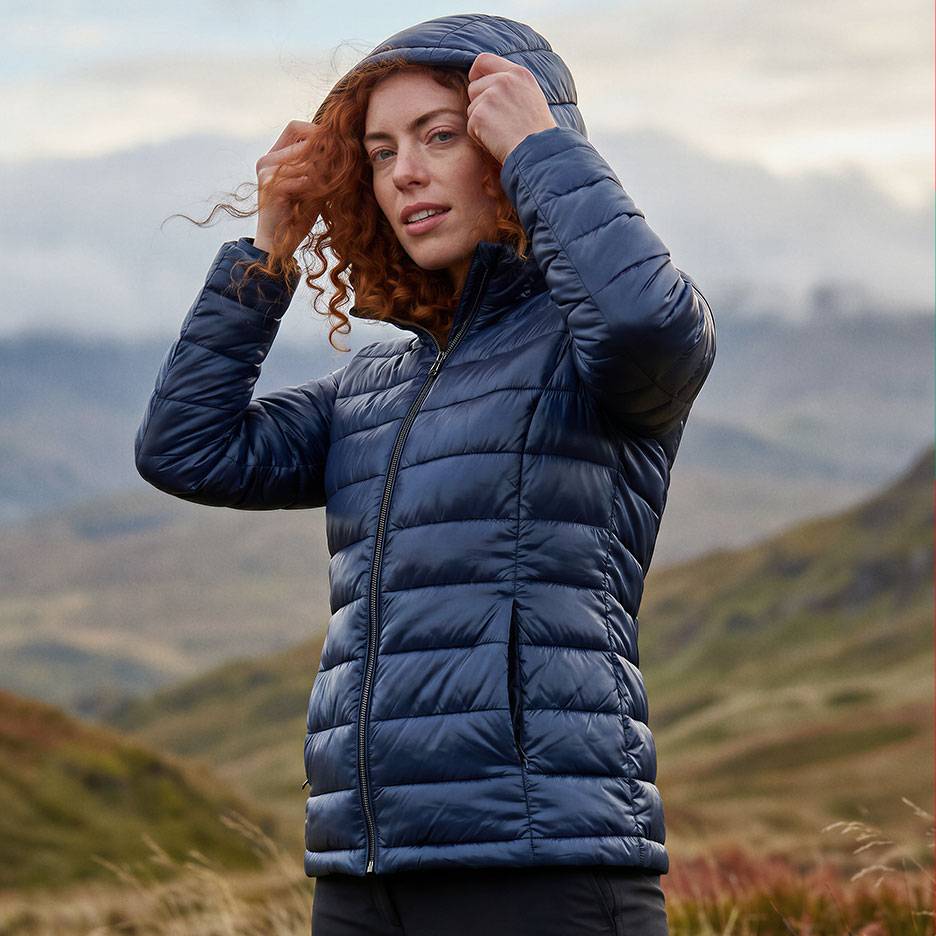 Donna con capelli rossi in un piumino blu scuro con cappuccio in un paesaggio montano.