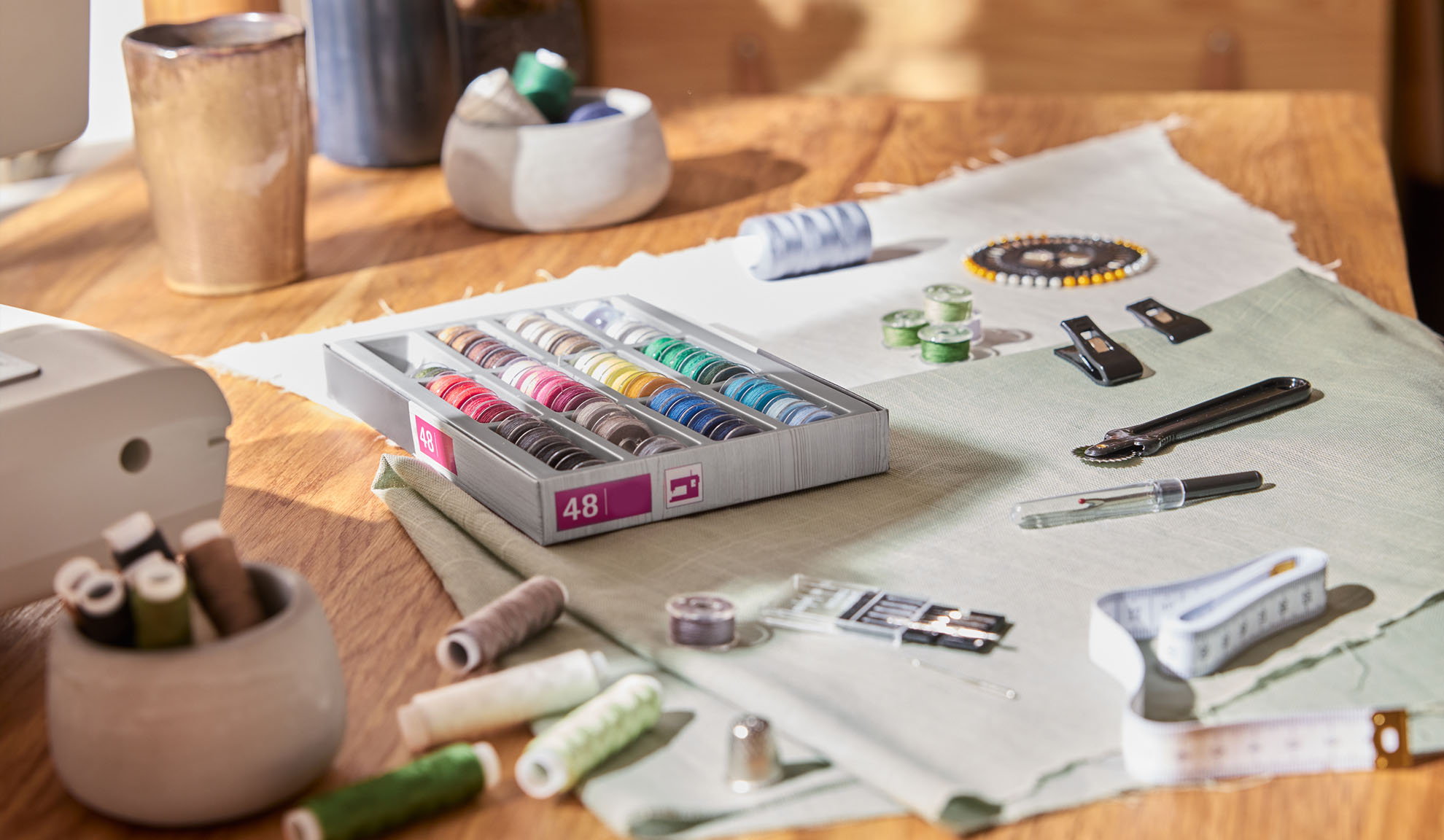 Kit da cucito con scatola di fili colorati, macchina da cucire e vari strumenti su un tavolo di legno.