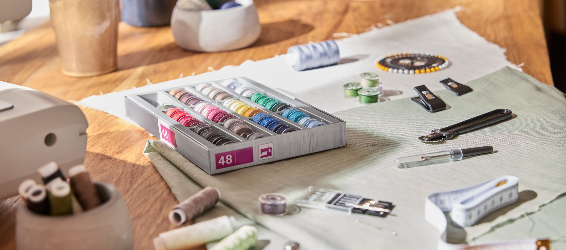 Articoli da cucito su un tavolo di legno, inclusi un organizer per fili con 48 rocchetti, tessuto e vari strumenti.