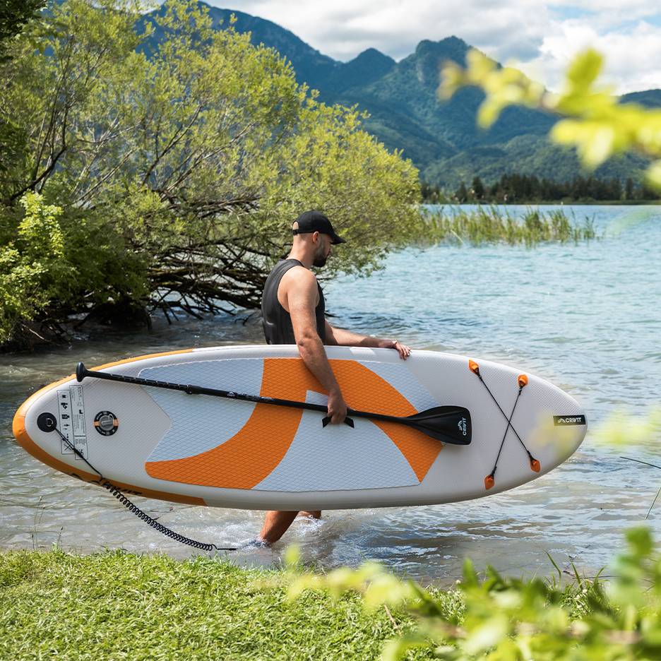 Uomo con tavola da SUP CRIVIT in acqua, pronto per pagaiare.