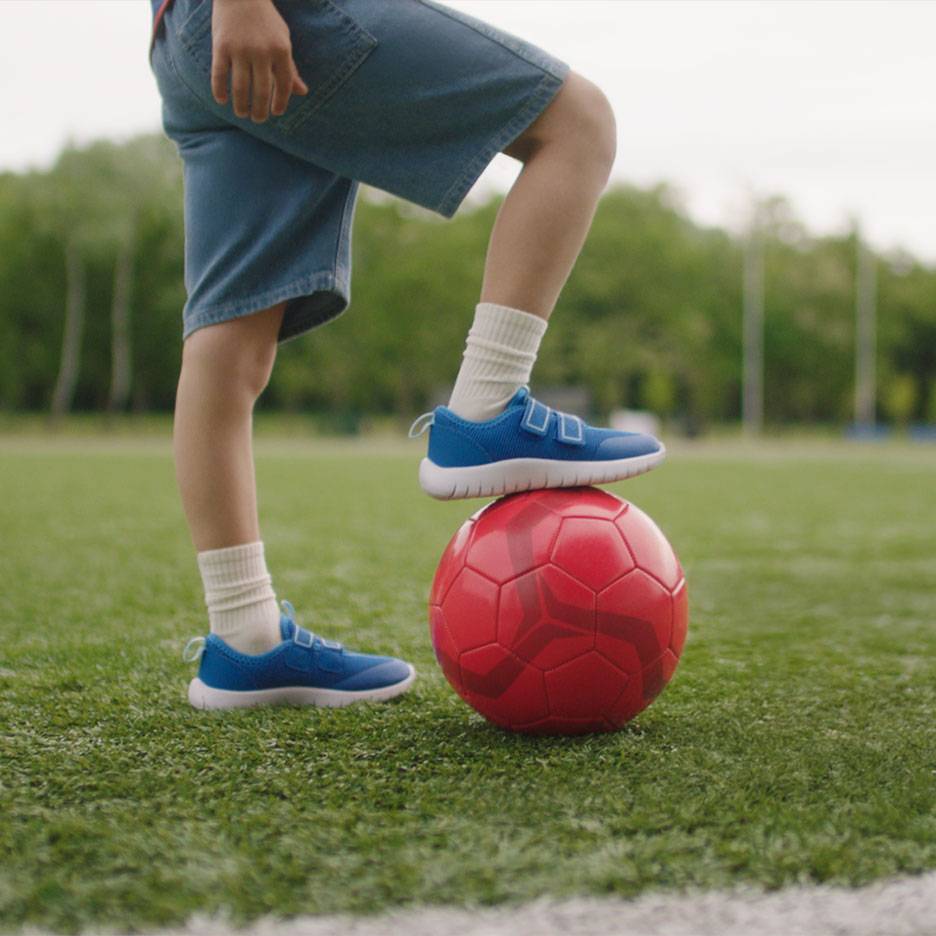 Bambino in pantaloncini e scarpe da ginnastica blu, con un piede su un pallone da calcio rosso.
