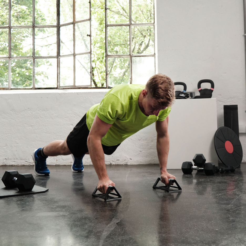 Uomo che fa flessioni con impugnature in palestra.