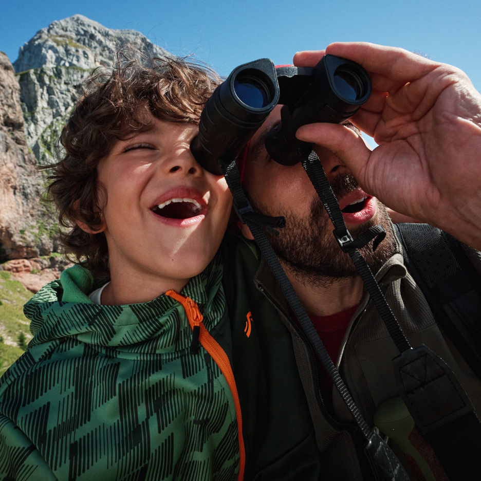 Padre e figlio esplorano le montagne con il binocolo, indossando giacche outdoor.