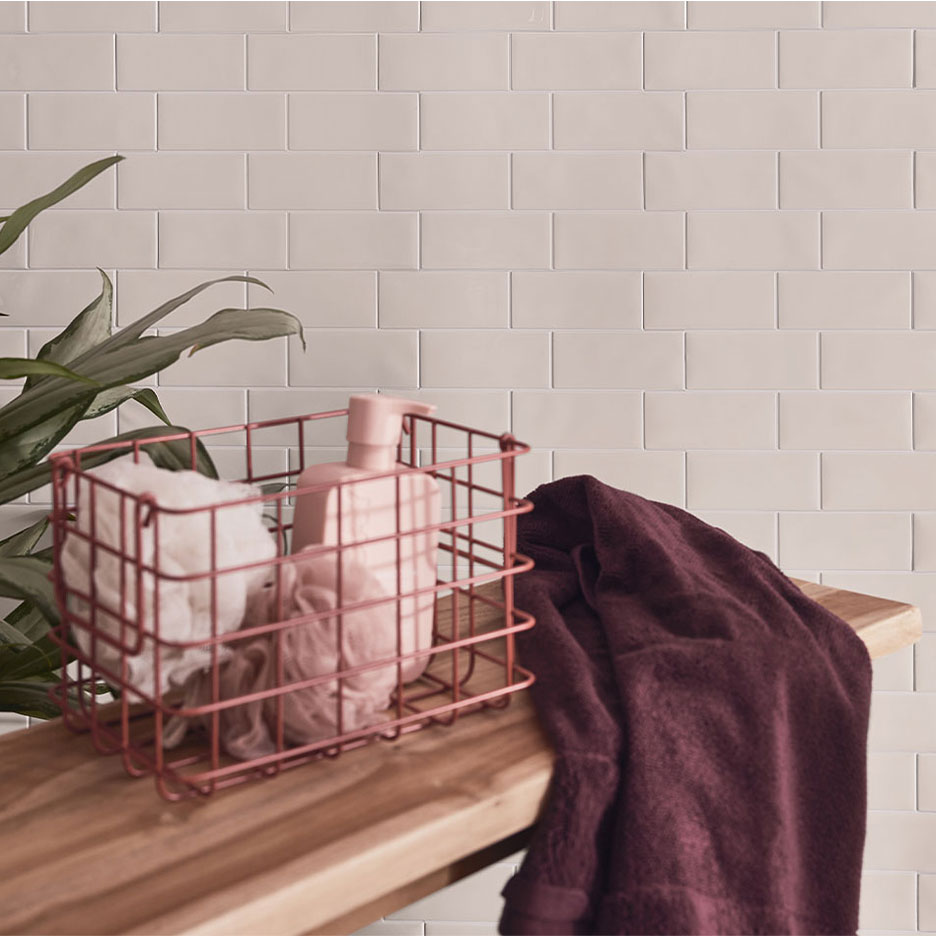 Arredamento bagno con piastrelle bianche, panca in legno, cesto con sapone e asciugamani.
