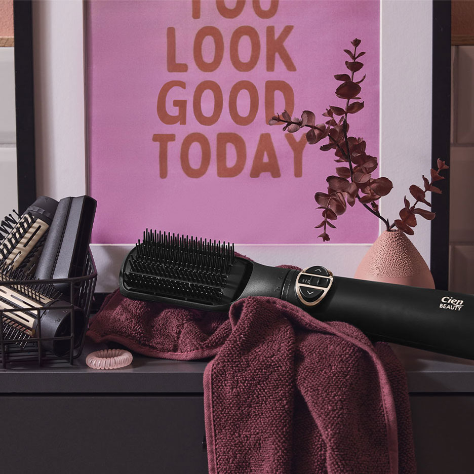 Spazzola lisciante Cien Beauty su un asciugamano, con accessori per capelli e un poster.