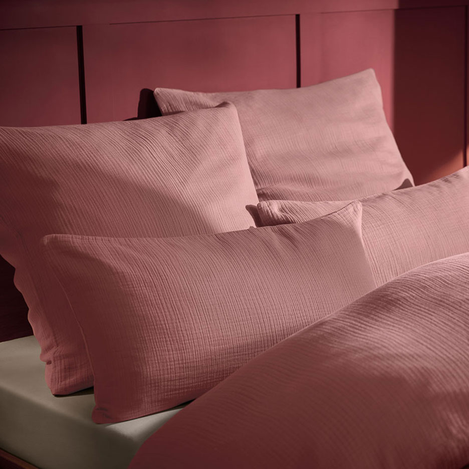 Cuscino e biancheria da letto in mussola rosa su un letto con testiera in legno.