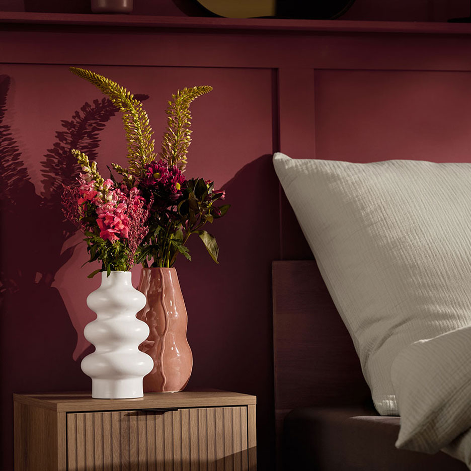 Due vasi con fiori su un comodino accanto a un letto con cuscino bianco.