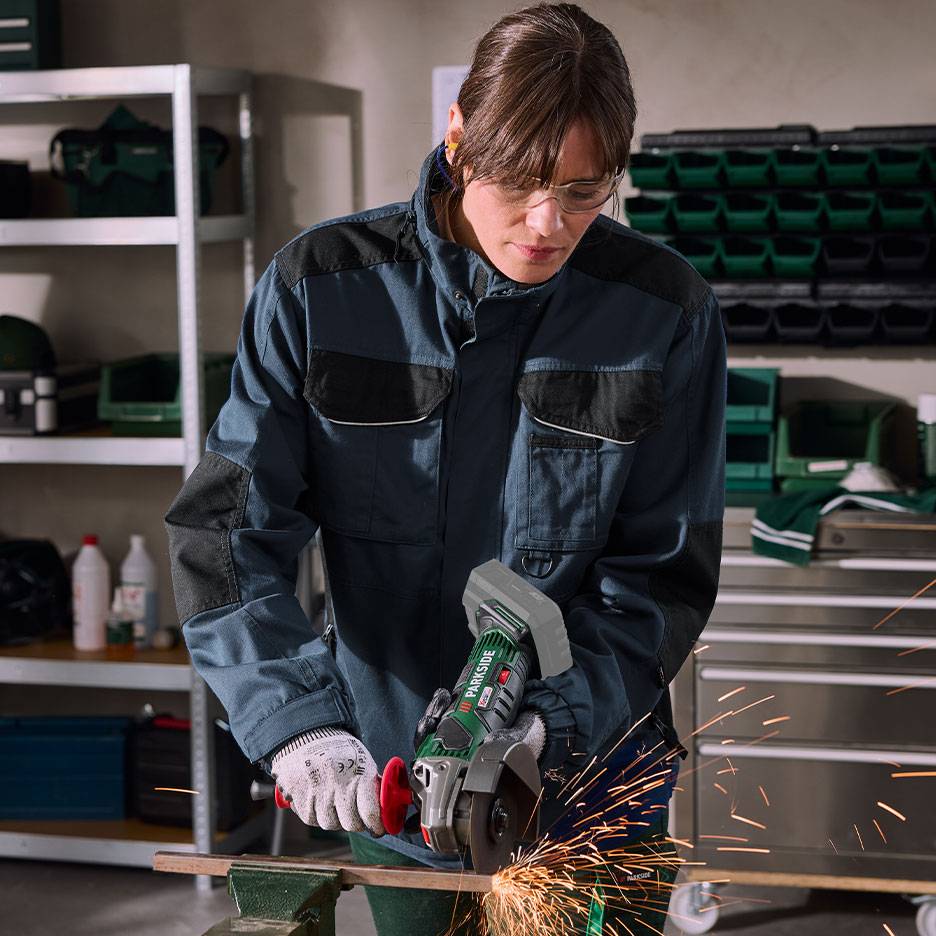 Donna con smerigliatrice angolare che taglia metallo, con scintille, in officina.