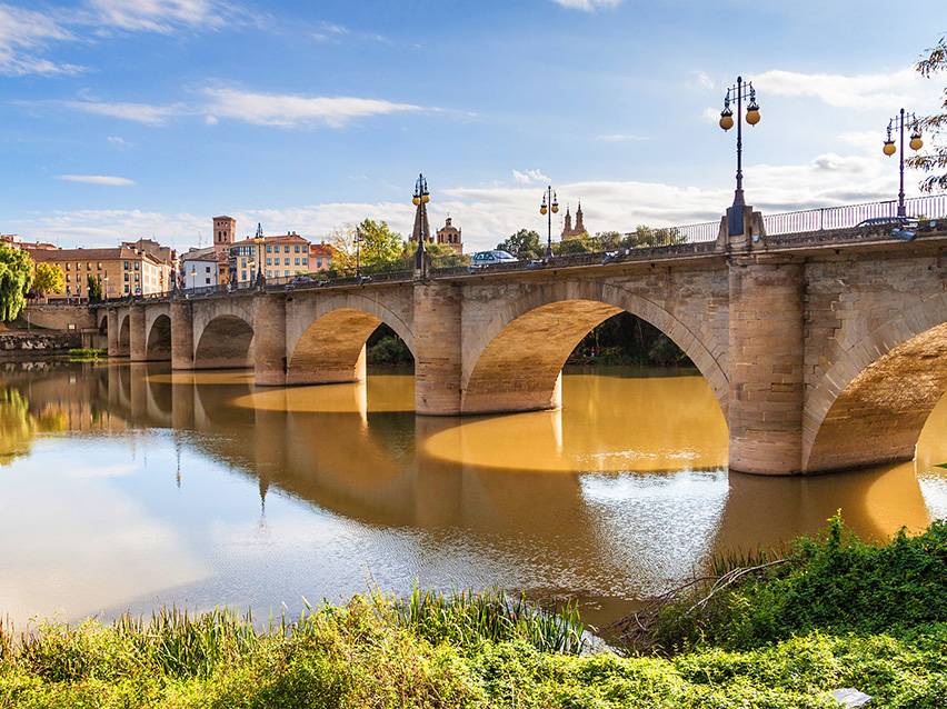 Ponte ad arco in pietra su un fiume con una città e cielo blu sullo sfondo.