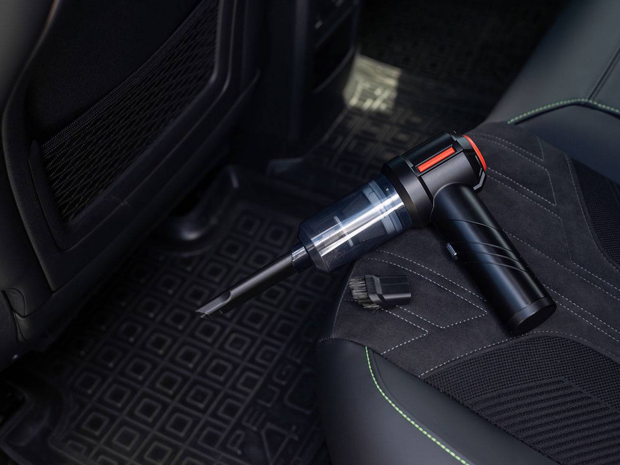 Aspirapolvere portatile compatto con accessori su un sedile dell'auto.