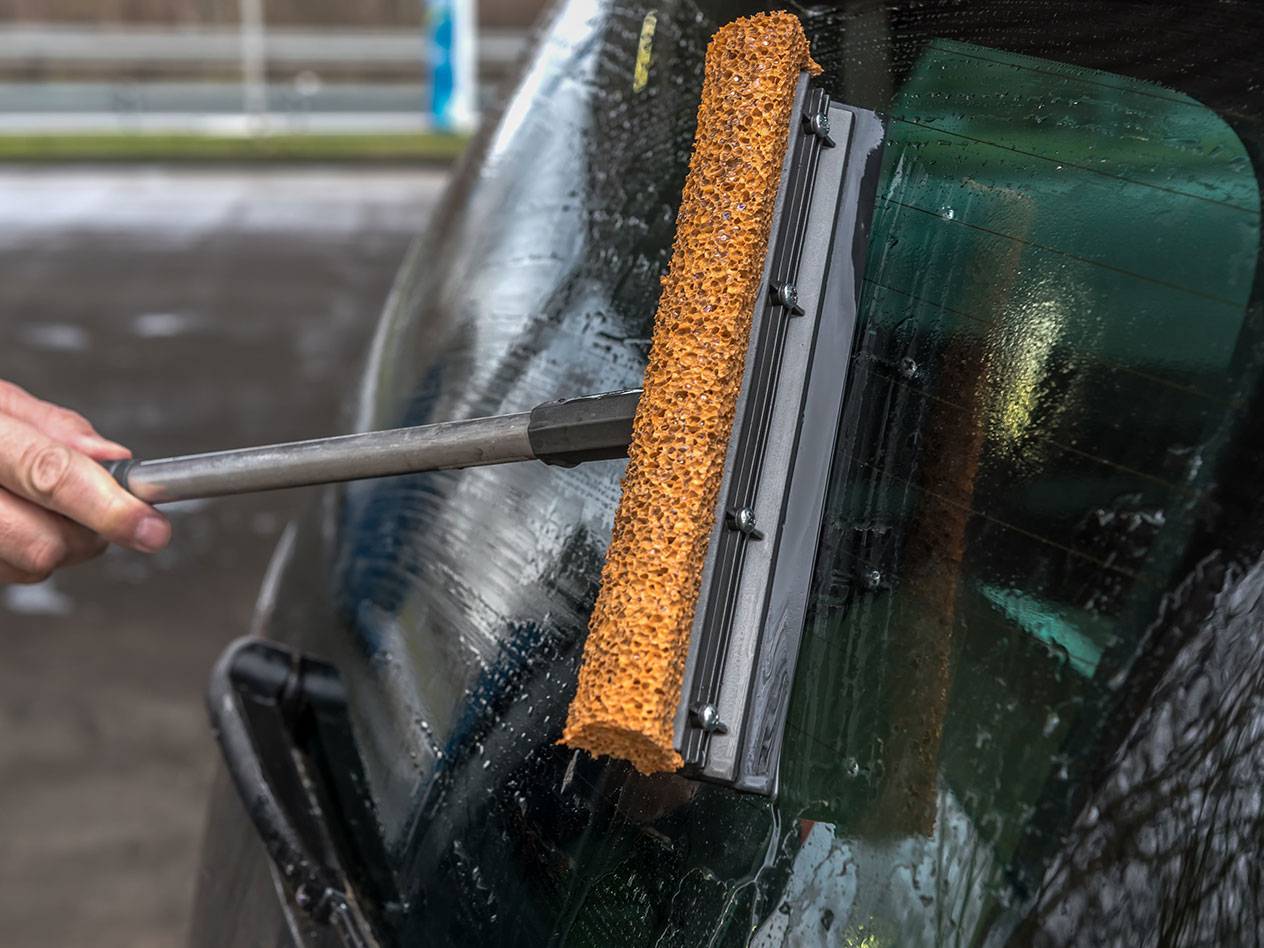 Lavavetri con manico lungo pulisce il lunotto di un'auto.