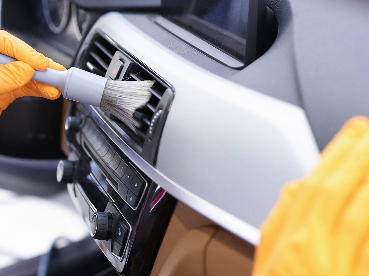 Pulizia degli interni di un'auto con una spazzola per dettagli e guanti di gomma.