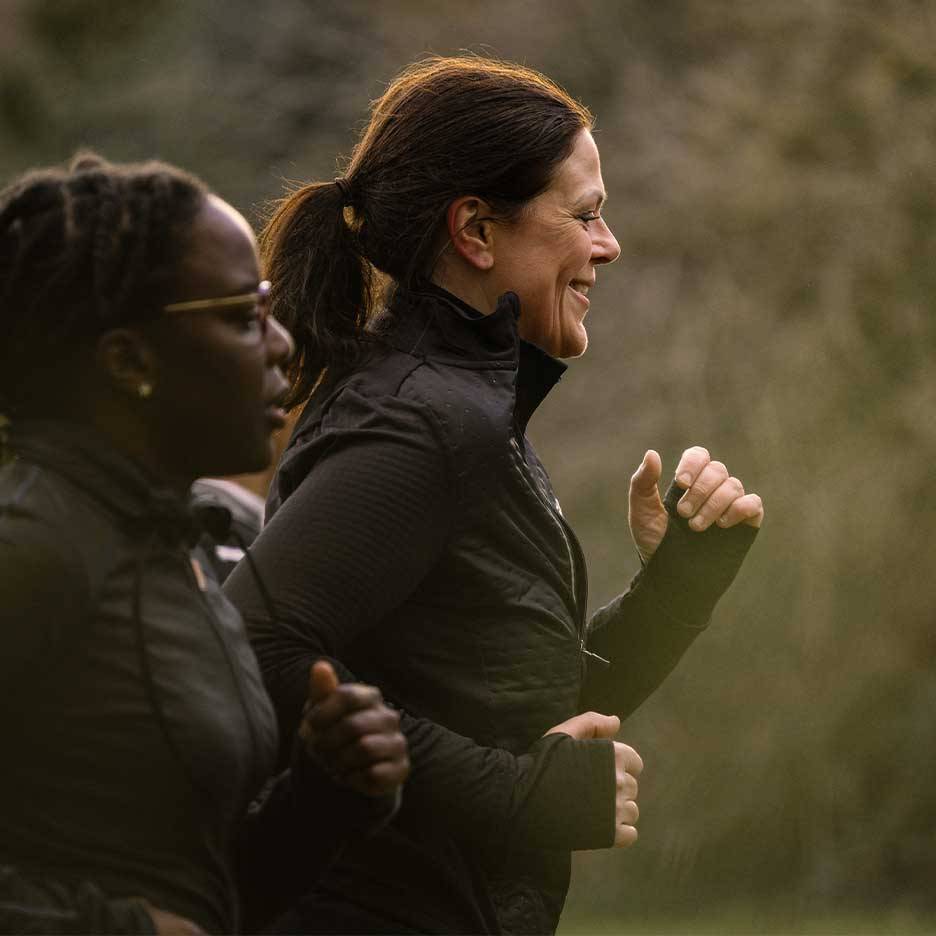Due donne in abbigliamento sportivo corrono all'aperto, una sorride.