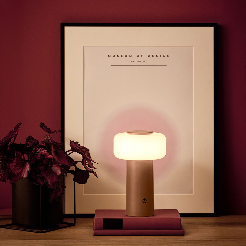 Lampada da tavolo portatile su libri, con pianta e poster sullo sfondo.