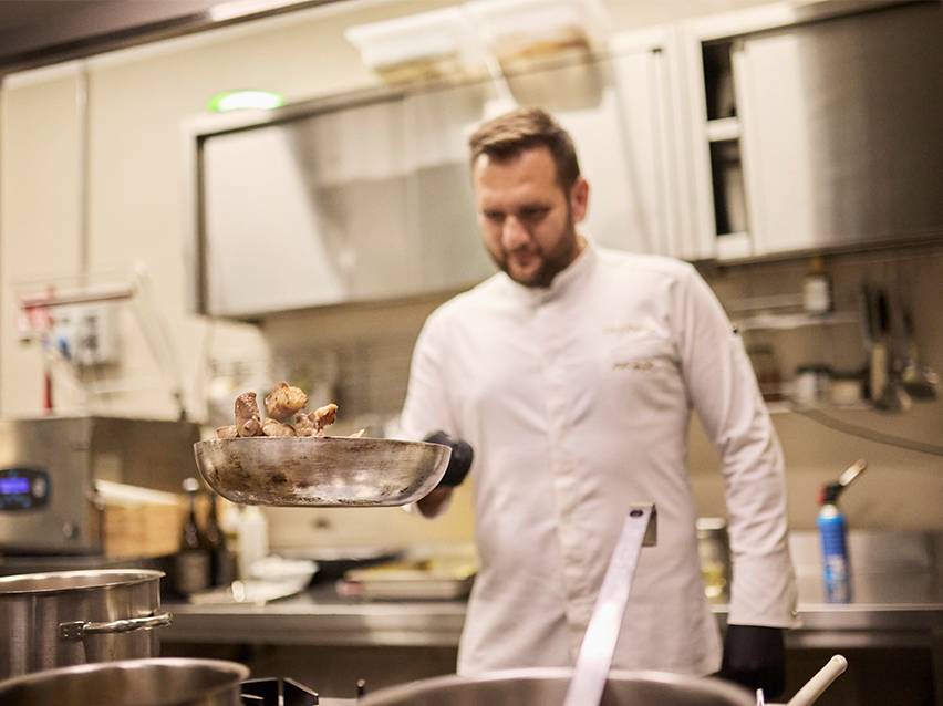 Un cuoco in giacca bianca che salta il cibo in padella.