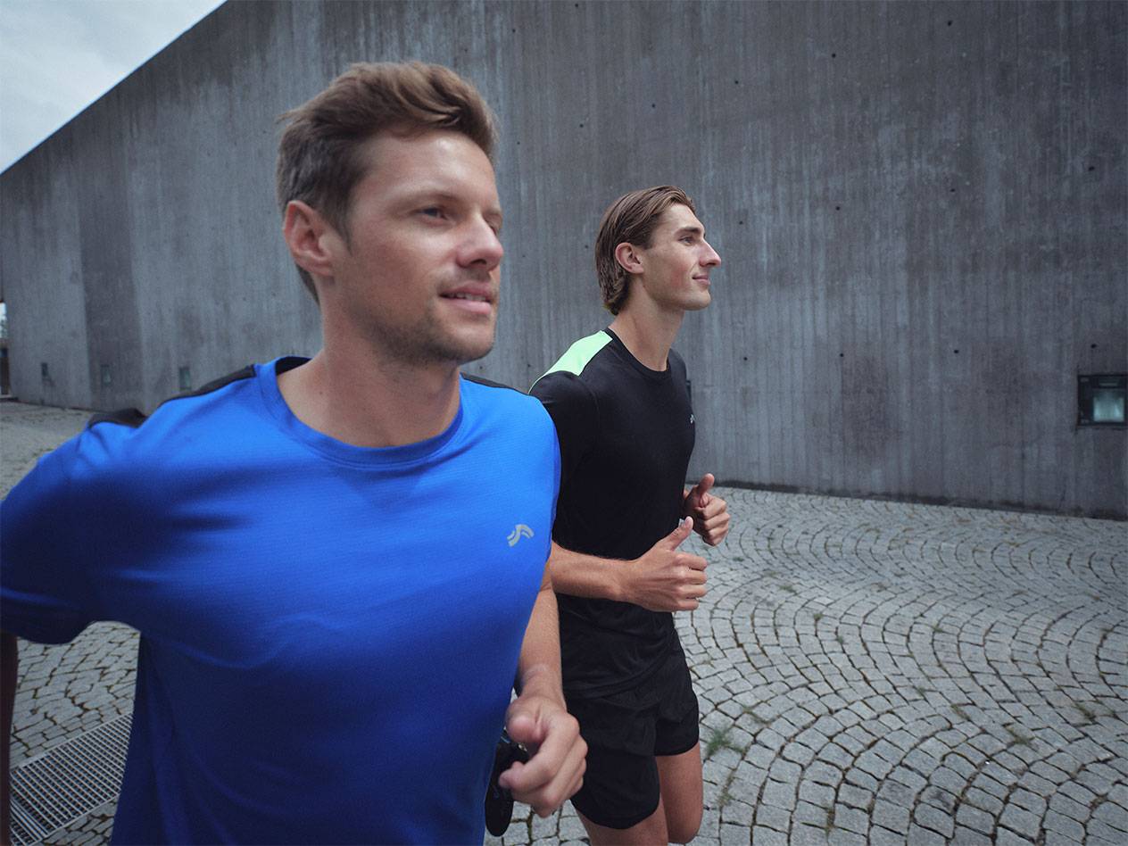 Due uomini corrono in magliette e pantaloncini sportivi, uno blu e uno nero.