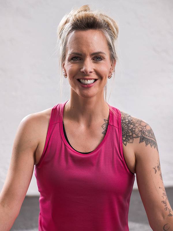 Una donna sorridente con canotta sportiva rosa e tatuaggi sulla spalla.