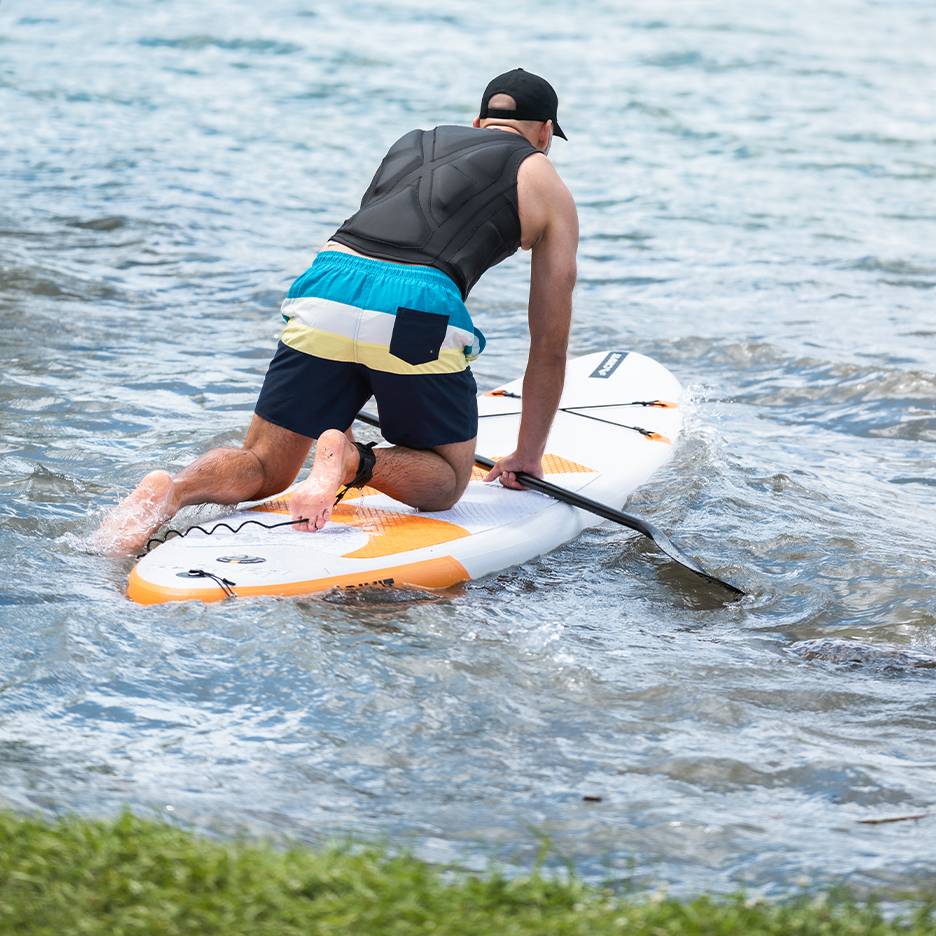 Uomo in ginocchio su una tavola da paddleboard con pagaia in acqua.