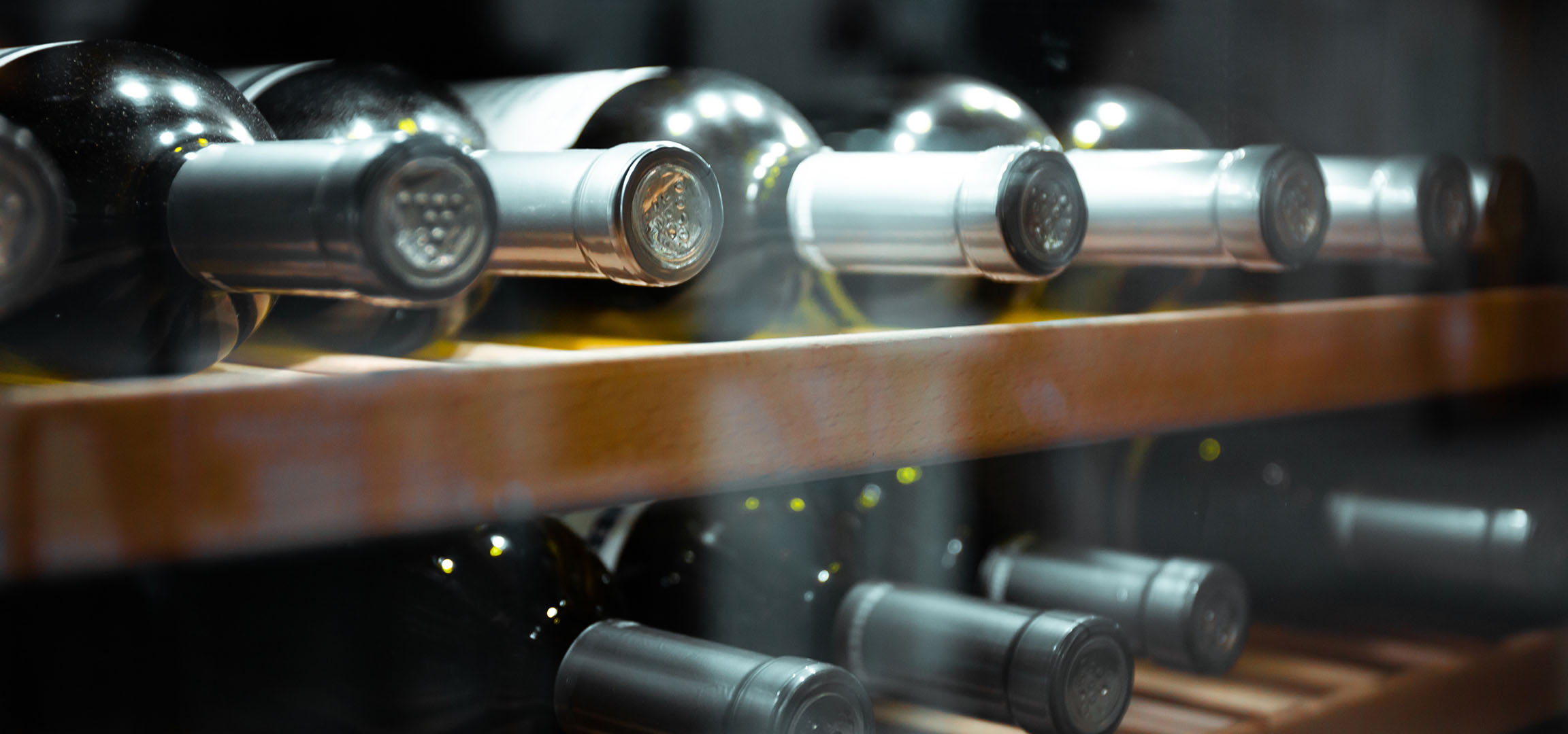 Primo piano di bottiglie di vino su uno scaffale di legno, che mostra i tappi e i riflessi.