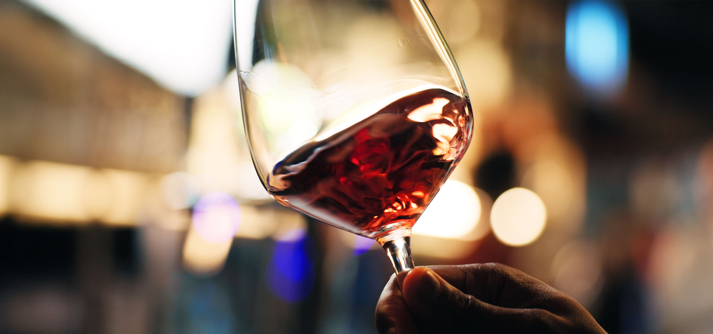 Primo piano di un bicchiere di vino rosso con luci sfocate sullo sfondo.